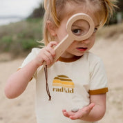Child holding a wooden toy on a beach 