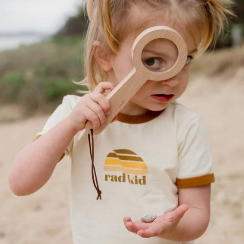 Child holding a wooden toy on a beach 