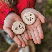 Two hands holding wooden discs with engraved text against a natural background