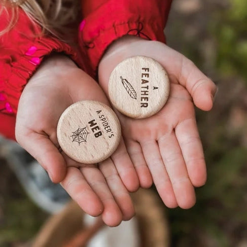 Two hands holding wooden discs with engraved text against a natural background